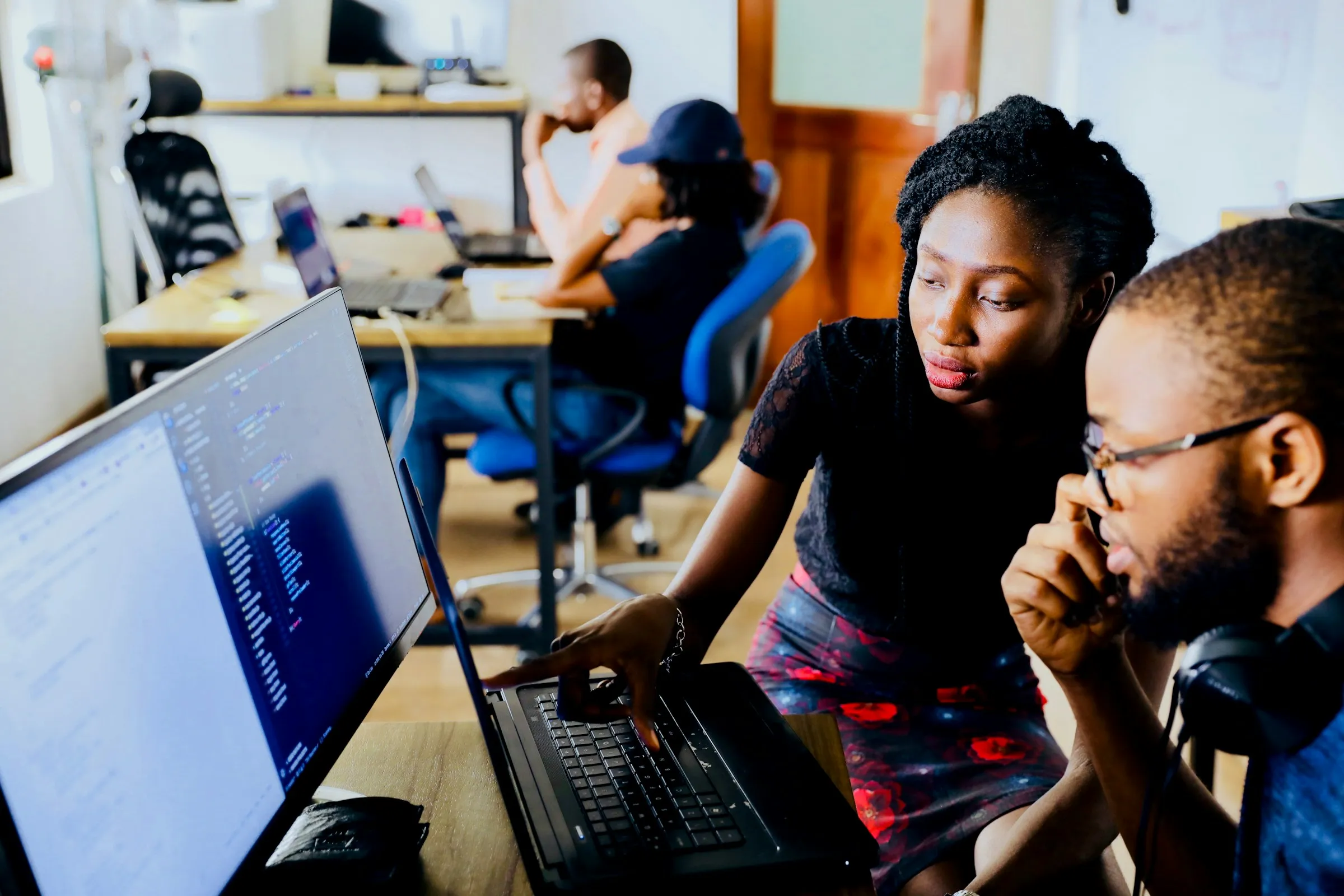 Mulher digitando em um notebook com colegas trabalhando ao fundo