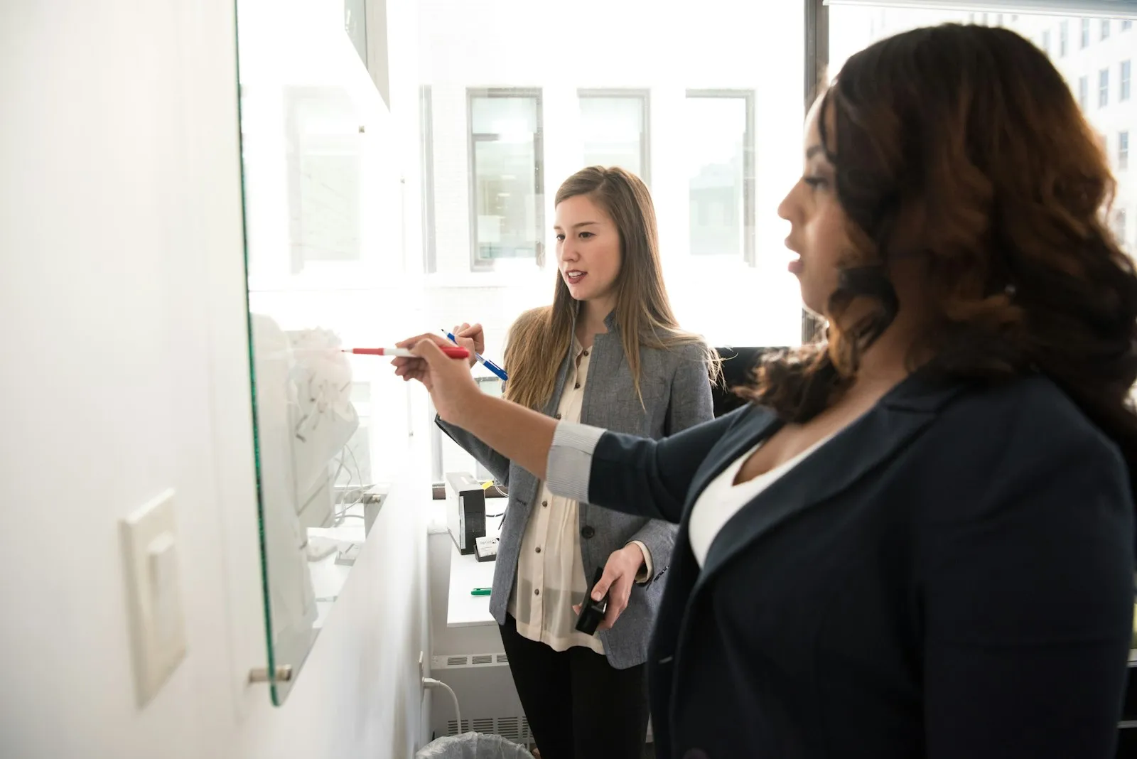 Mulher liderando uma reunião de trabalho em frente a um quadro branco